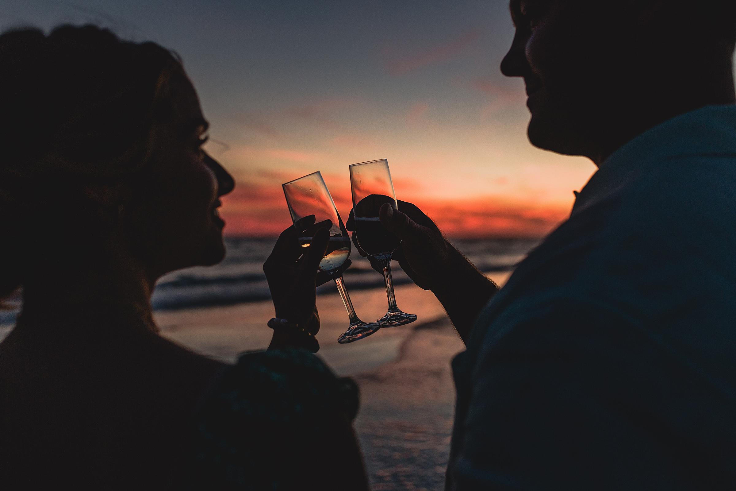 couple clinking glasses during sunset at engagement session on siesta key beach