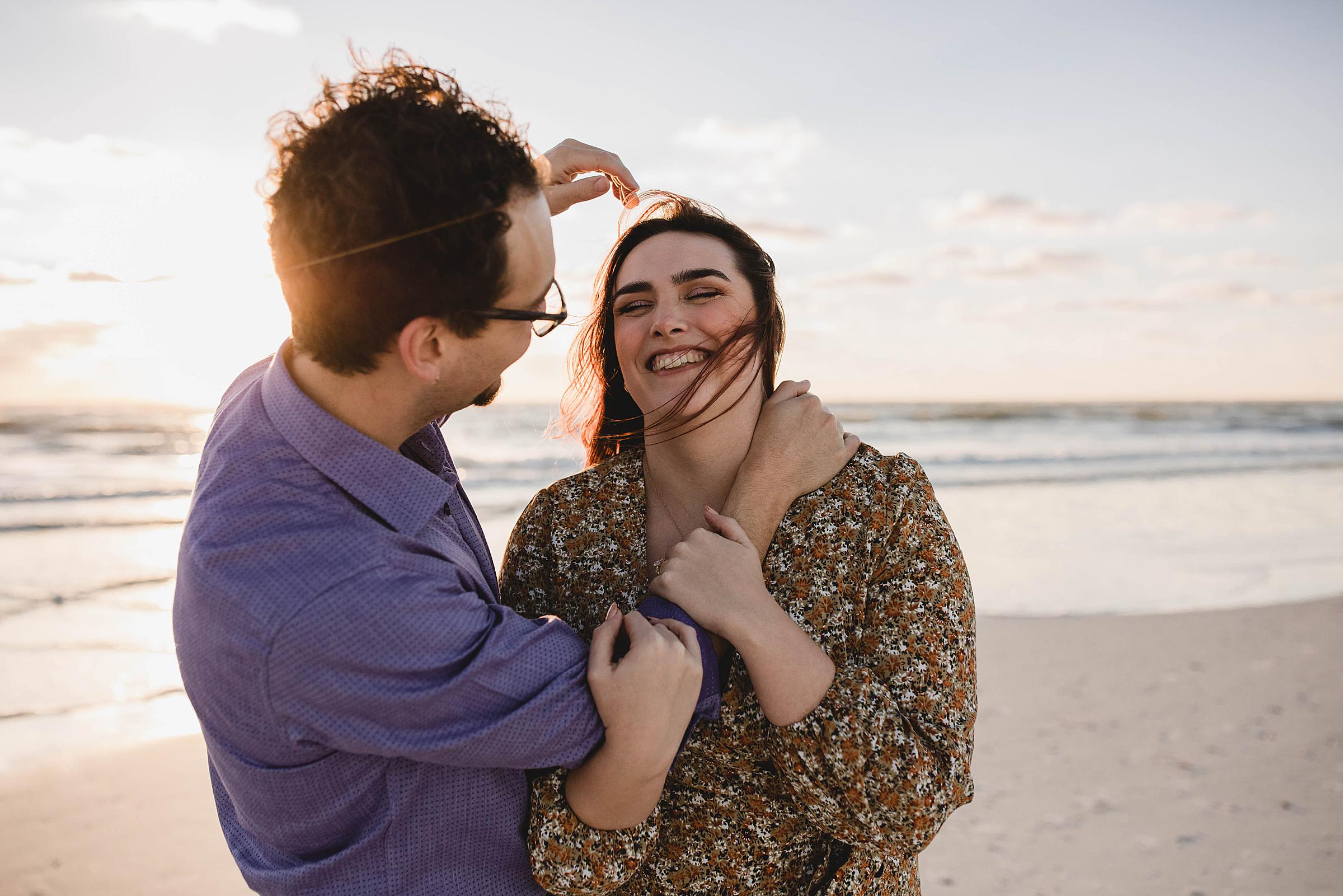 Couple laughing and fixing eachother's hair on Lido Beach at engagement session
