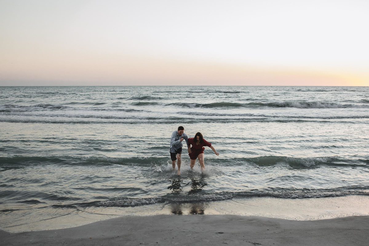 couple running out of the water on the beach during sunset at longboat key florida engagement session by juliana montane photography