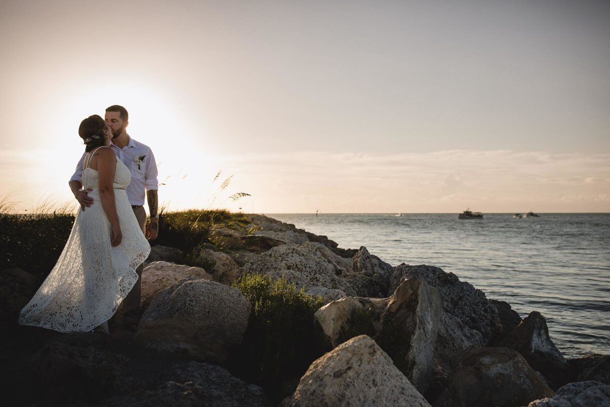bride and groom kissing on the rocks near the ocean at clearwater beach elopement photographed by juliana montane photography