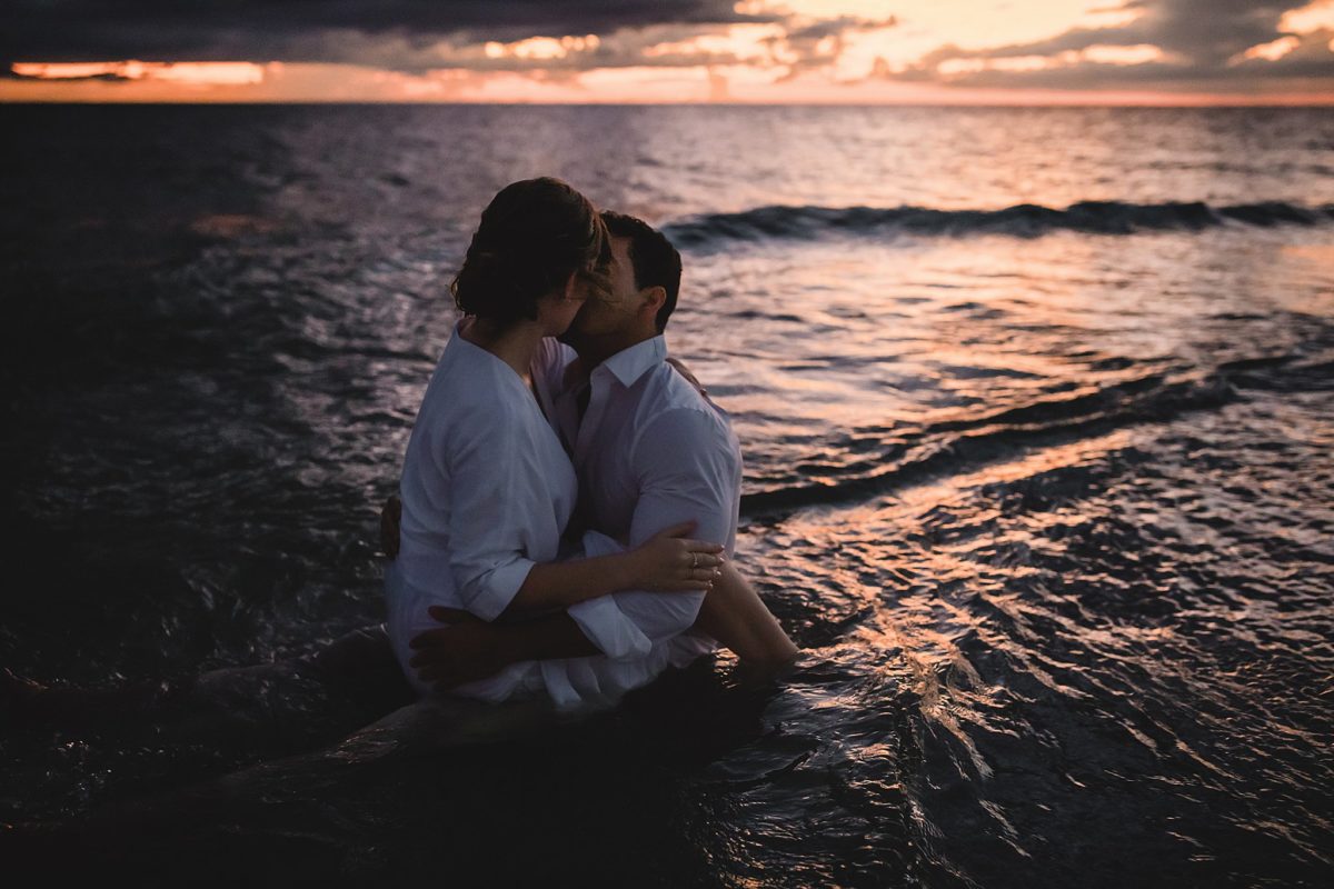 couple sitting in the ocean kissing, sarasota engagement photo session photographed by juliana montane photography