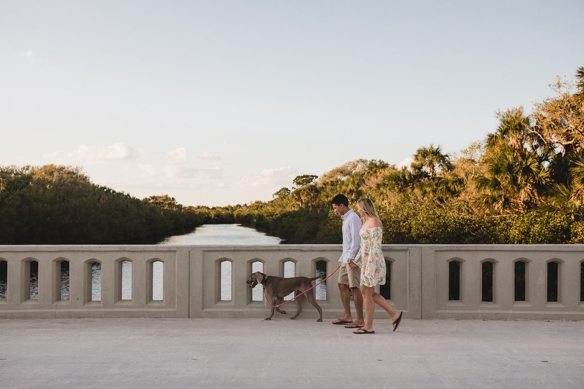 Couple walking across a bridge to caspersen beach with their dog during engagement session photoshoot