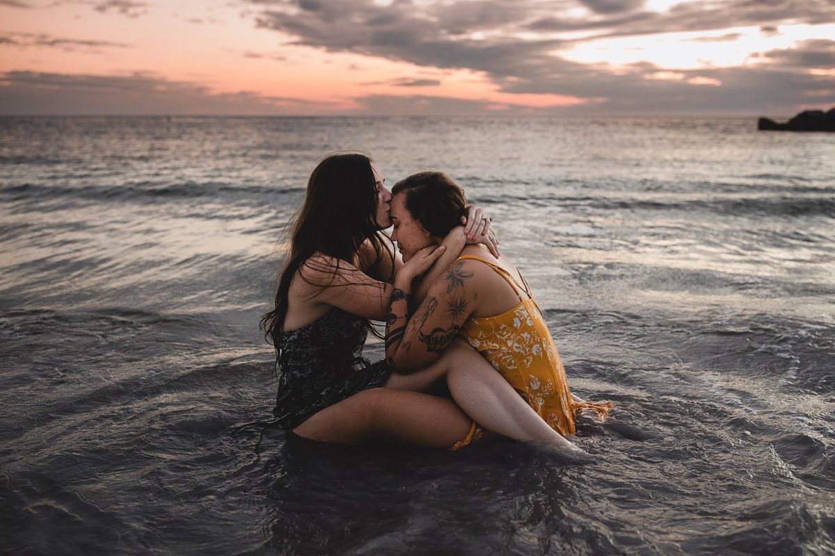 Female couple kissing sitting in the water at st pete beach during engagement session