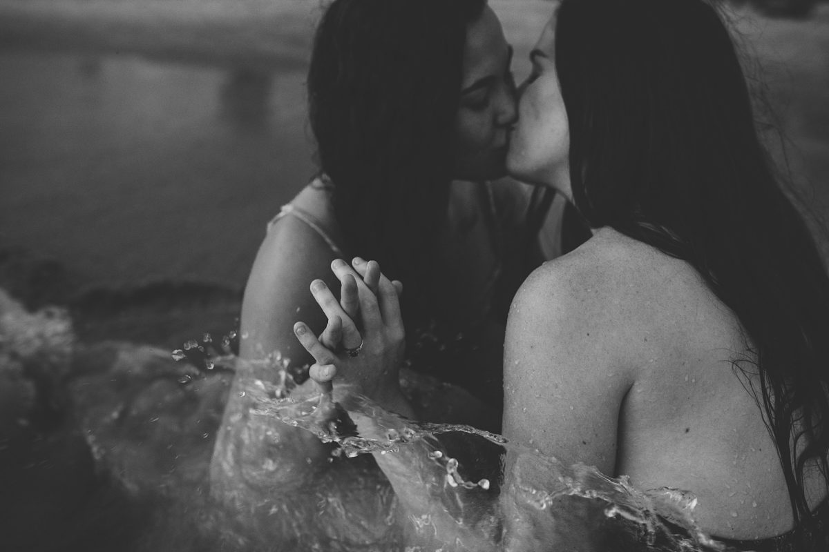 same sex female couple kissing sitting in the water at st pete beach during engagement session