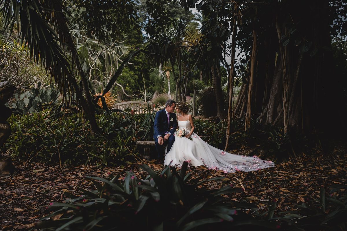 bride and groom sitting on a bench in marie selby botanical gardens during their wedding