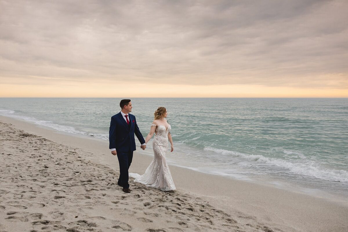 Bride and groom walking down turtle beach holding hands and looking at the sunset in sarasota florida, wedding photography by juliana montane photography