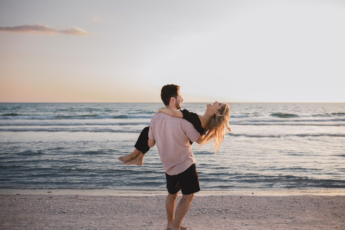 man holding woman and spinning around after getting engaged on siesta key beach in sarasota florida photographed by Juliana Montane Photography