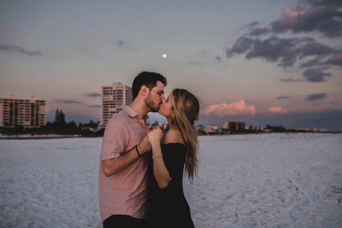 Newly engaged couple kissing with the full moon behind them on siesta key beach in sarasota florida photographed by Juliana Montane Photography