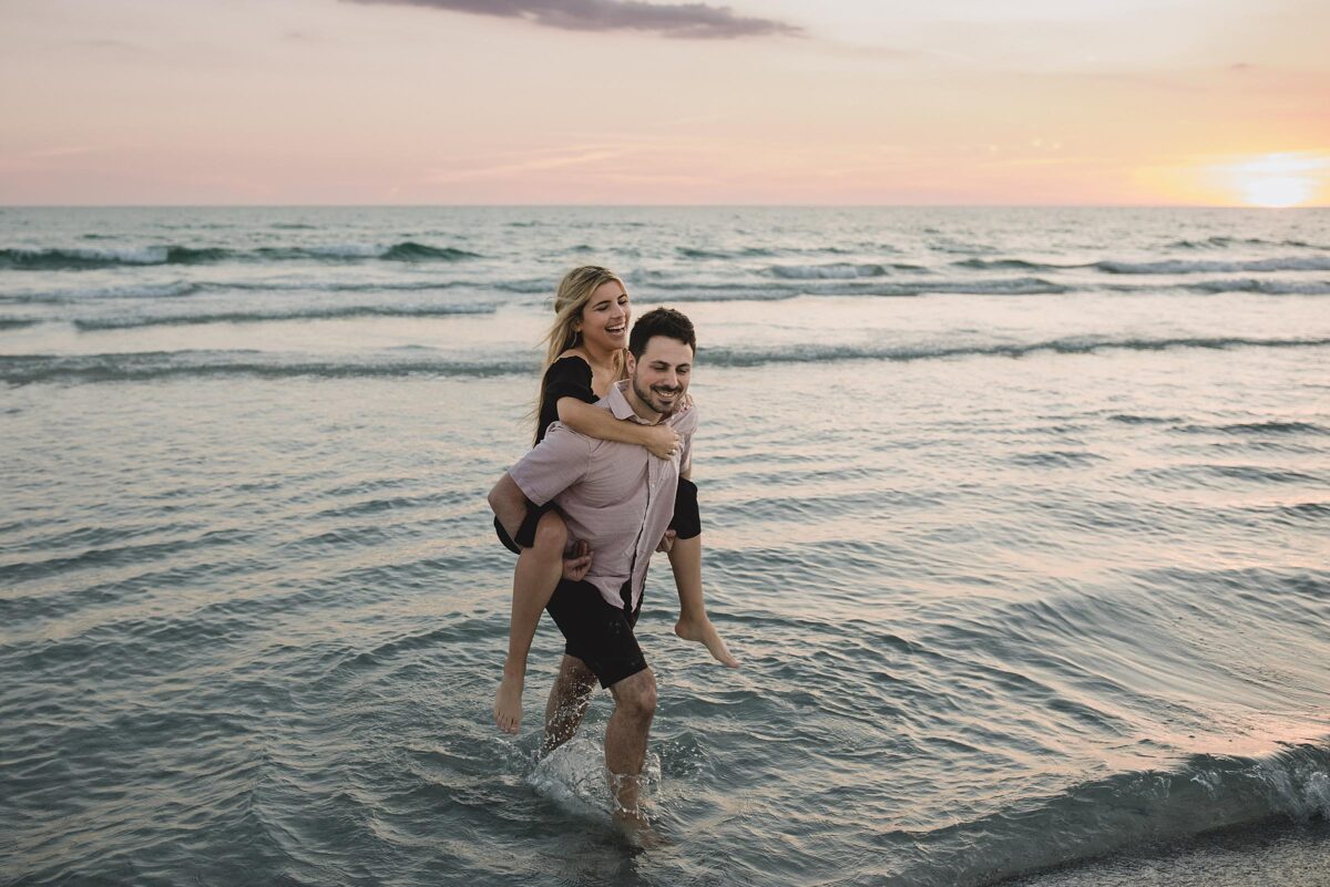 woman riding on man's back during photography session after man proposed on siesta key beach in sarasota florida photographed by Juliana Montane Photography