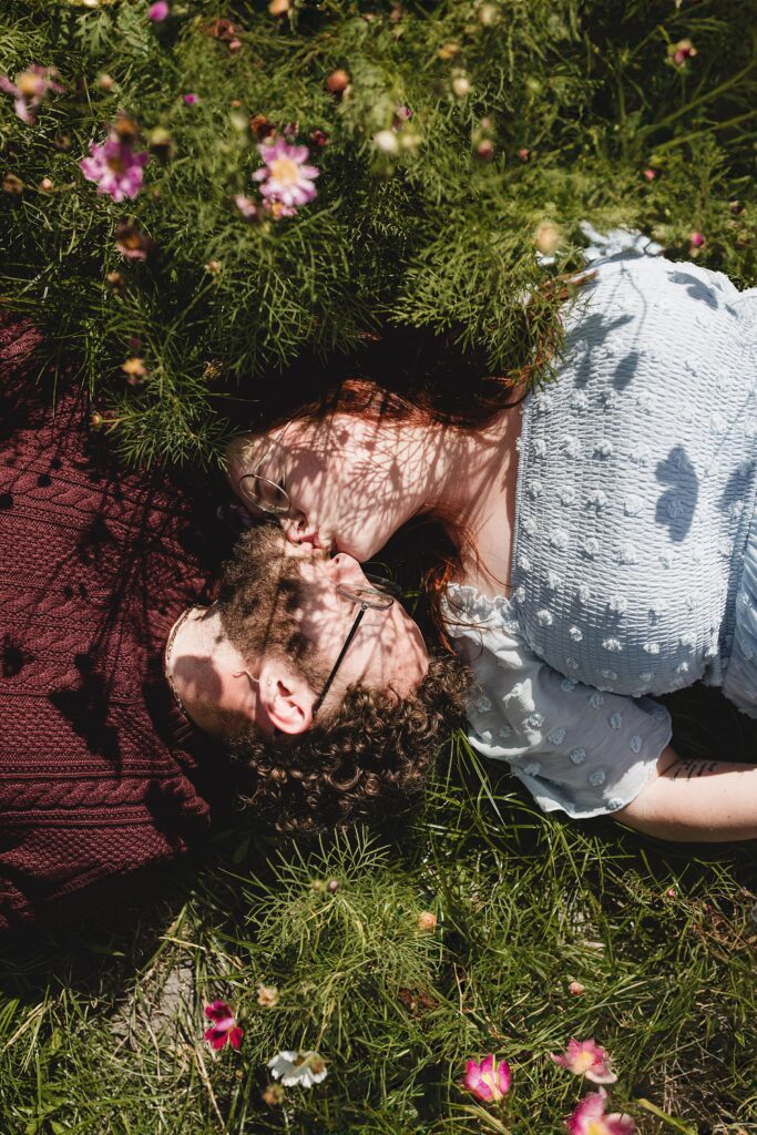 Newly engaged couple laying in a flower field at Hunsader Farm.Photographed by Juliana Montane Photography.