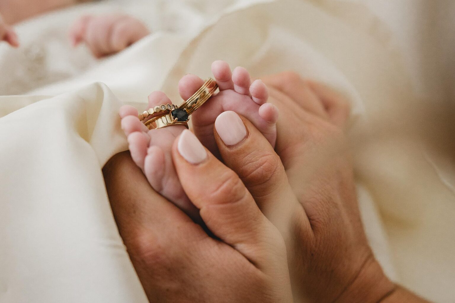 Bride holding the feet of her 2 month with their wedding bands on the baby's toes. Photographed by Juliana Montane Photography.