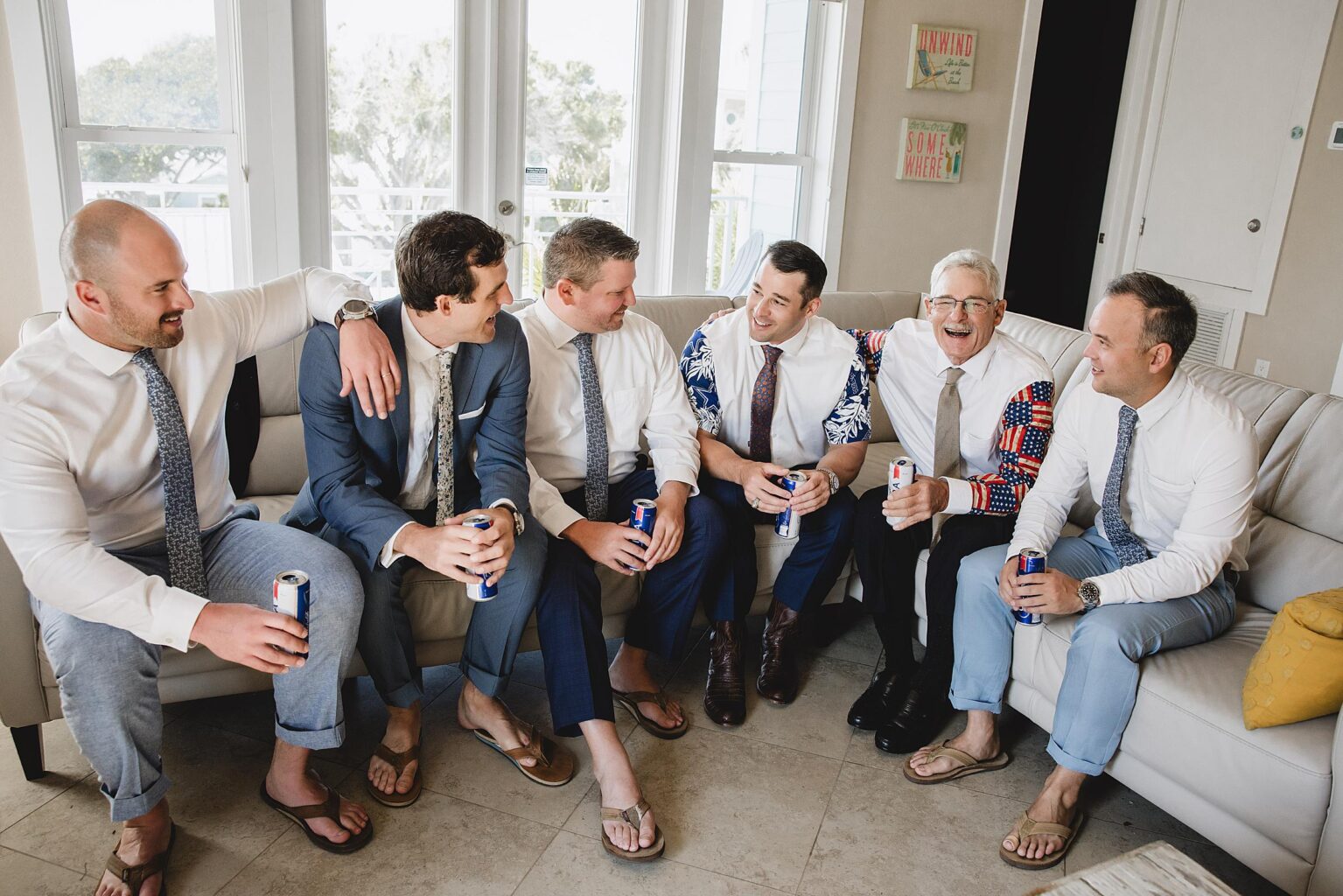 Groomsmen hanging out on a couch drinking beer, getting ready for a wedding on Bradenton Beach, FL. Photographed by Juliana Montane Photography.