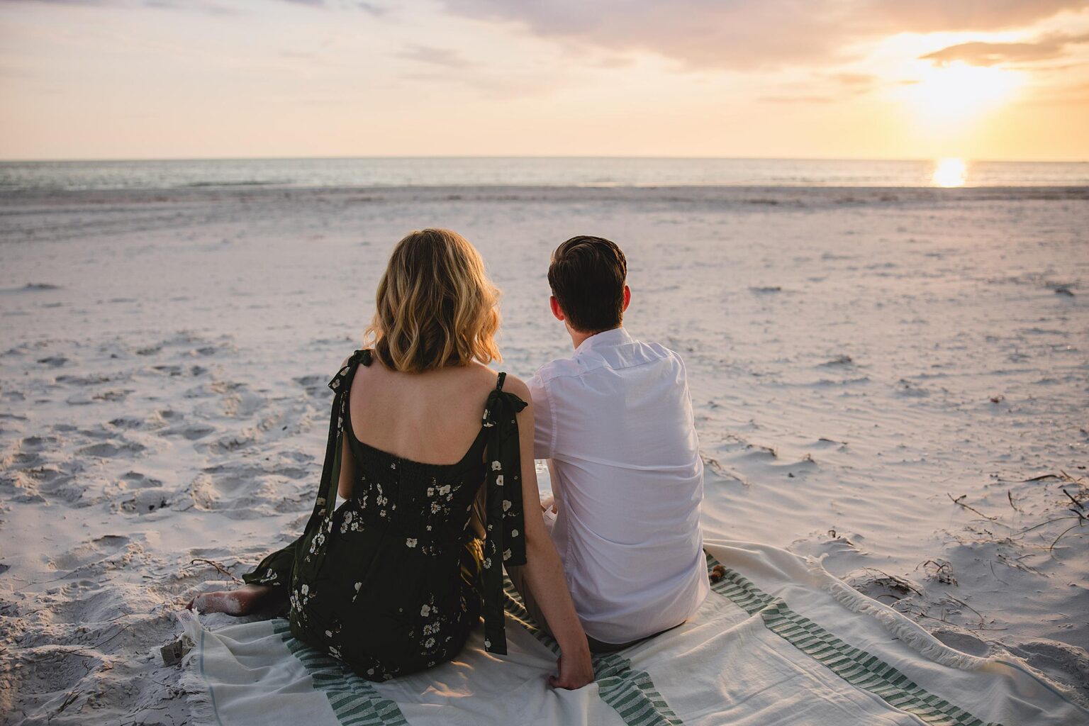 Newly engaged couple look out at the water on Siesta Key Beach in Florida. Photographed by Juliana Montane Photography.