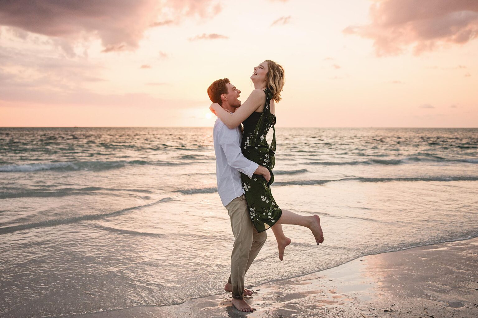 Man lifting woman up and laughing on the beach at siesta key in florida. Photographed by Juliana Montane Photography.