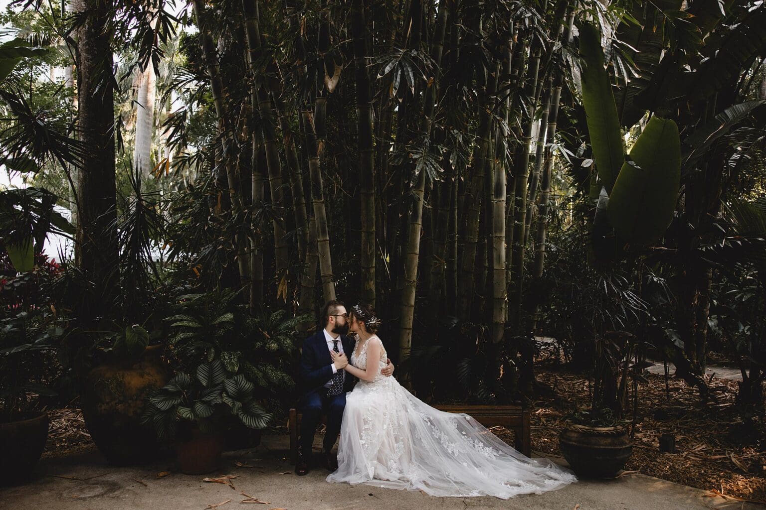 Bride & Groom sitting on a bench surrounded by bamboo trees at a Sunken Gardens Wedding in St. Petersburg, FL photographed by Juliana Montane Photography