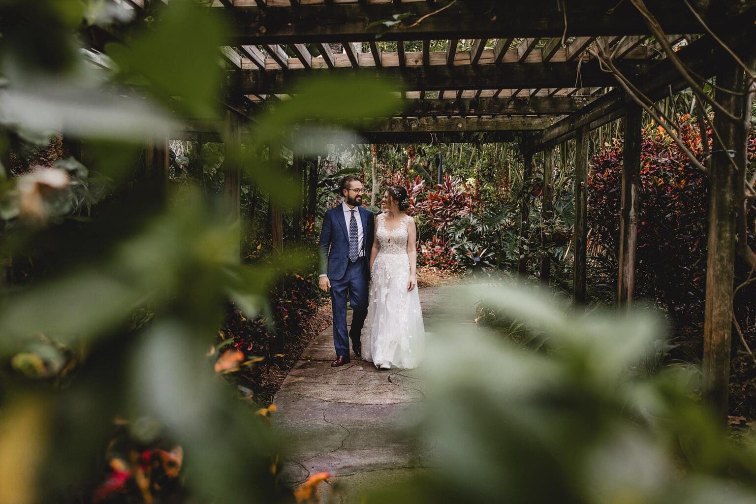 Bride & Groom walking through the gardens under a pergola  at a Sunken Gardens Wedding in St. Petersburg, FL photographed by Juliana Montane Photography