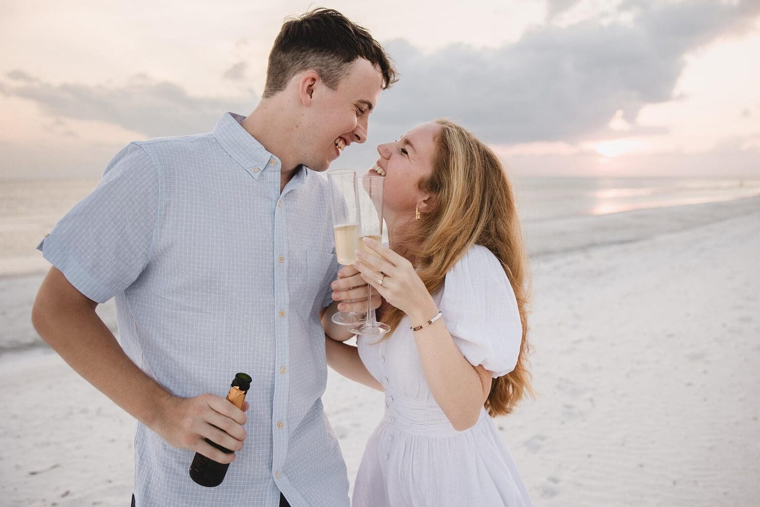 Newly engaged couple celebrating with champagne on Longboat Key Beach after their sunset surprise proposal in Sarasota, FL photographed by Juliana Montane Photography