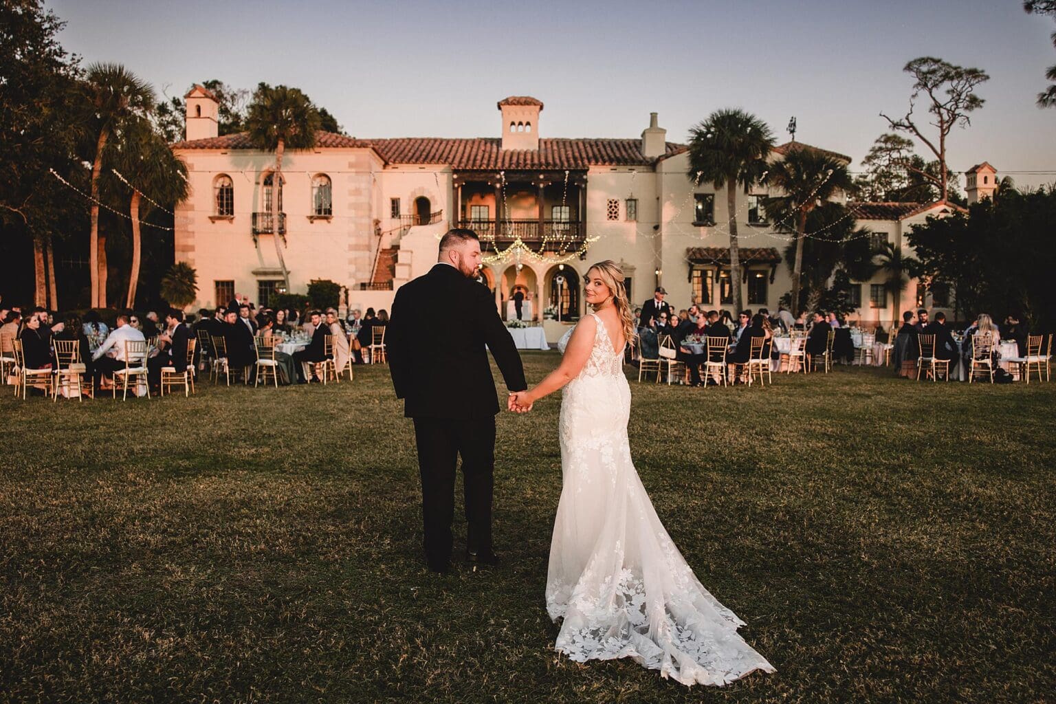 Bride & Groom walking towards the mansion from Sarasota Bay at sunset at a Crosley Mansion wedding in Sarasota Florida photographed by Juliana Montane Photography