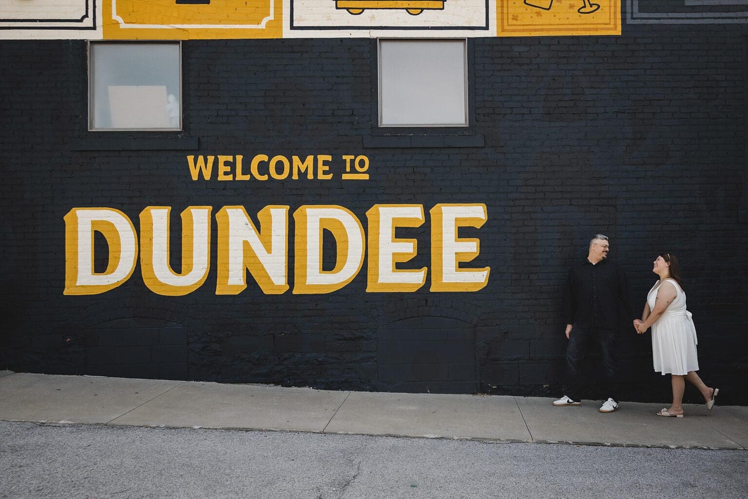 Couple walking in front of Dundee mural in historic Dundee in Omaha, NE photographed by Juliana Montane Photography